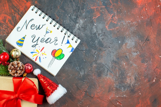 Bezpłatne zdjęcie widok z góry mały prezent związany z czerwoną wstążką gałąź drzewa bożego narodzenia nowy rok napisany w notatniku na ciemnoczerwonym stole wolne miejsce