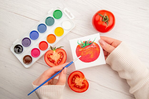 Widok z góry mały rysunek pomidora z pomidorami i kolorowymi farbami na białym stole
