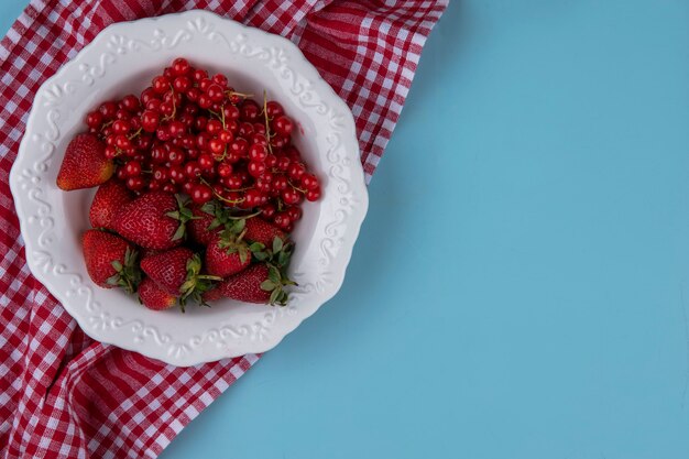 Widok z góry miejsca na kopię truskawki z czerwoną porzeczką na talerzu z czerwonym ręcznikiem kuchennym na jasnoniebieskim tle