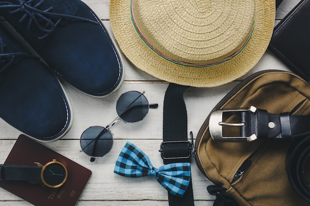 Widok z góry na akcesoria podróżujące z koncepcją odzieżową. krawat dziobu, portmonetka na drewnianych background.watch, okulary słoneczne, torba, kapelusz i buty na stół drewna.