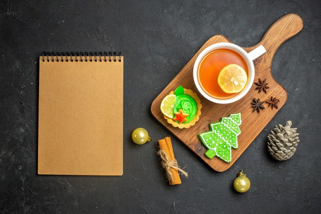 Widok z góry na filiżankę czarnej herbaty noworoczne akcesoria szyszek iglasty i limonki cynamonowe obok notebooka na czarnym tle