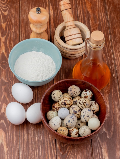 Bezpłatne zdjęcie widok z góry na jajka przepiórcze na drewnianej misce z mąką na niebieskiej misce z octem jabłkowym z białymi jajami kurzymi na drewnianym tle