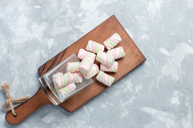 Widok z góry na jasnobiałym biurku, kolorowe pyszne pianki marshmallows, małe cukierki.