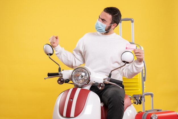 Widok z góry na koncepcję podróży z dumnym facetem w masce medycznej siedzącej na motocyklu z żółtą walizką na nim i trzymającym kartę bankową
