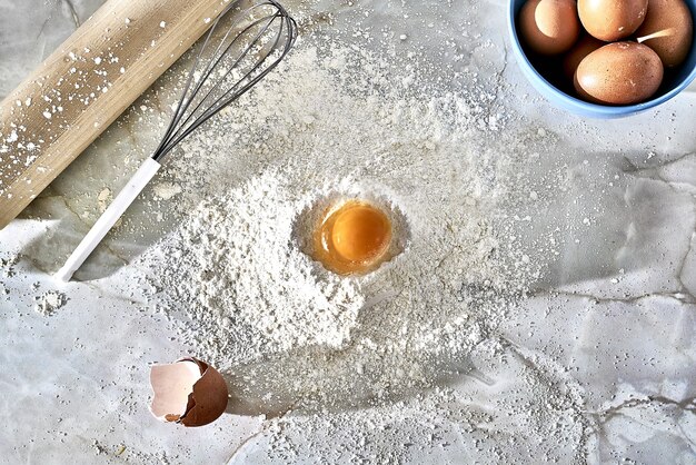 Widok z góry na kopiec podłogi z jajkiem, trzepaczką i drewnianym wałkiem do ciasta