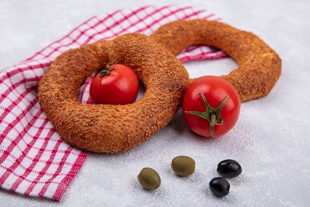 Bezpłatne zdjęcie widok z góry na miękkie tradycyjne tureckie bułeczki ze świeżymi pomidorami i oliwkami na czerwonym szmatką sprawdzane na białym tle