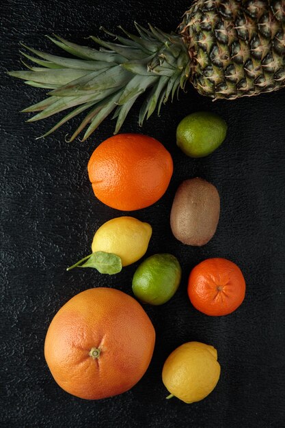 Widok z góry na owoce cytrusowe jako ananas z pomarańczową cytryną kiwi i limonką na czarnym tle