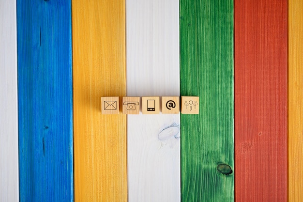 Widok z góry na pięć drewnianych kostek z ikonami kontaktu i komunikacji. na kolorowym tle drewnianych desek.