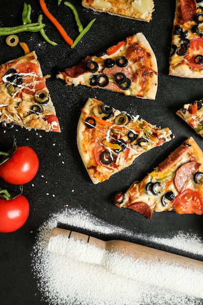 Widok z góry na pizzę z pomidorami, oliwkami i papryką na czarnym stole