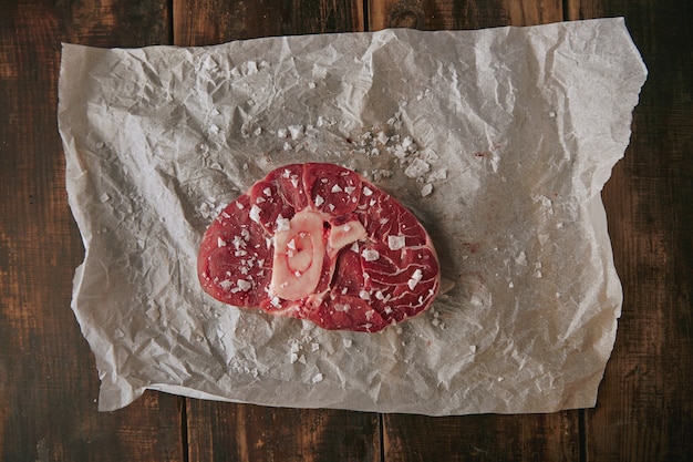 Widok z góry na stek solony surowego mięsa na papierze rzemieślniczym na grubym szczotkowanym starym drewnianym stole grunge