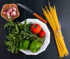Bezpłatne zdjęcie widok z góry na surowe spaghetti z pomidorami miętowymi i papryką w talerzu z nożem i czosnkiem na czarnej powierzchni