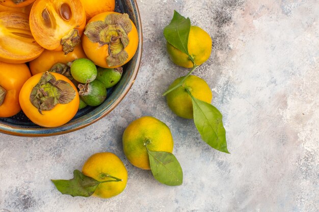 Widok z góry na świeże persimmons feykhoas w misce i mandarynki na nagim tle