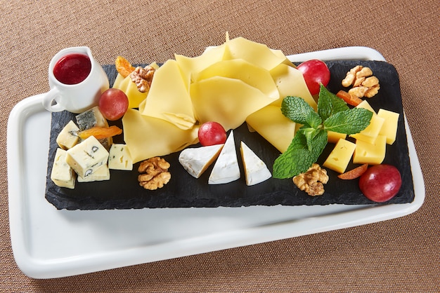 Widok z góry na talerz serów z serem Gouda brie blue cheese, orzechami włoskimi, winogronami i słoikiem dżemu