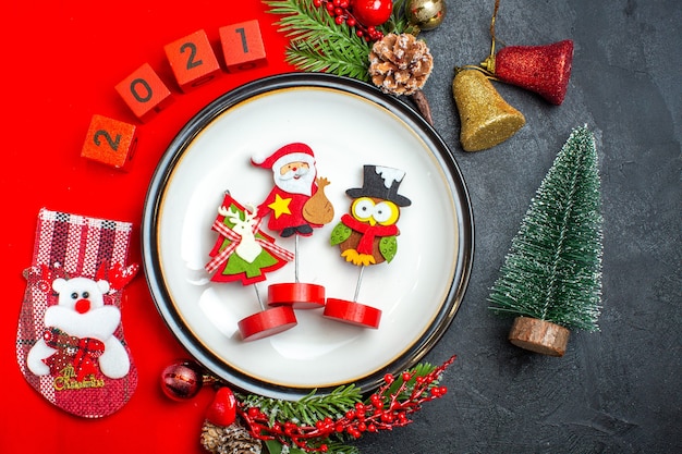 Widok z góry na tło nowego roku z akcesoriami do dekoracji talerza obiadowego gałęzie jodły i numery Świąteczna skarpeta na czerwonej serwetce obok choinki na czarnym stole