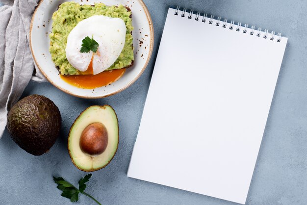 Widok z góry notebooka z tostem z awokado na talerzu i jajkiem w koszulce na wierzchu