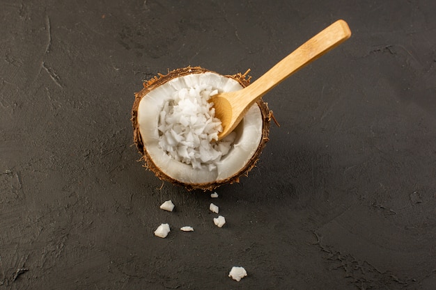 Bezpłatne zdjęcie widok z góry owoc kokosowy pokrojony w połowę drewnianą łyżką wewnątrz miąższu na szarym tle owoce egzotyczne mleko