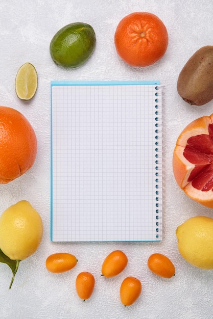 Widok z góry owoców cytrusowych wokół notatnika jako pomarańczowy limonkowy kumkwat cytrynowy grejpfrut kiwi na białym tle