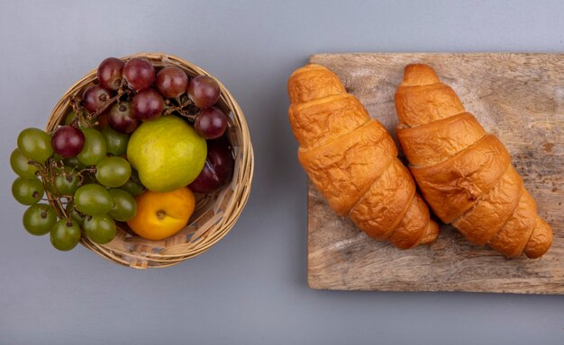 Widok z góry owoców jako pluot nectacot winogronowy w koszu i rogaliki na deska do krojenia na szarym tle