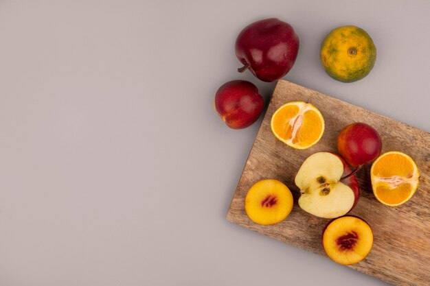 Widok z góry owoców, takich jak brzoskwinie, jabłka i mandarynki na białym tle na drewnianej desce kuchennej na szarej ścianie z miejsca na kopię