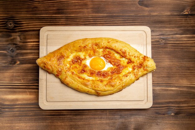 Widok z góry pieczony chleb z gotowanym jajkiem na brązowej powierzchni drewnianej chleb bułka jedzenie jajko ciasto śniadaniowe