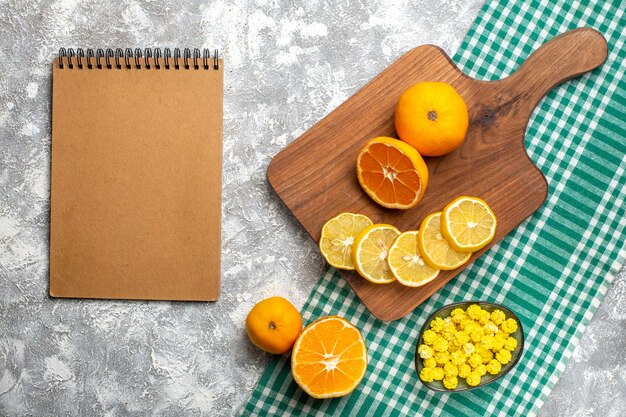 Widok z góry pomarańcze plasterki cytryny na desce pomarańcze żółte cukierki w misce na zielonym białym obrusie w kratkę notatnik na szarym stole