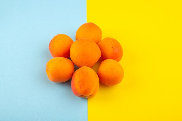 Widok z góry pomarańczowe brzoskwinie kwaśne smaczne świeże płody wyłożone lodowo-niebiesko-żółtym tłem owoców egzotycznego letniego soku