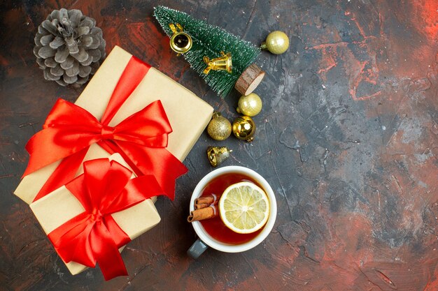 Widok z góry prezenty świąteczne złote kulki świąteczne filiżanka herbaty mini choinka na ciemnoczerwonym stole wolne miejsce