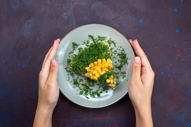 Widok z góry pyszna sałatka z majonezem, kukurydzą i kurczakiem wewnątrz talerza na ciemnej podłodze.