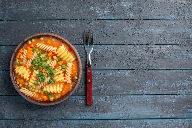 Widok z góry pyszna zupa makaronowa ze spiralnego włoskiego makaronu z zielenią na ciemnym rustykalnym daniu obiadowym na biurku włoski sos do zupy makaronowej