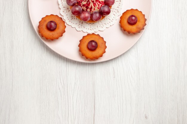 Widok z góry pyszne ciasta z winogronami wewnątrz płyty na białym stole, ciasto deserowe