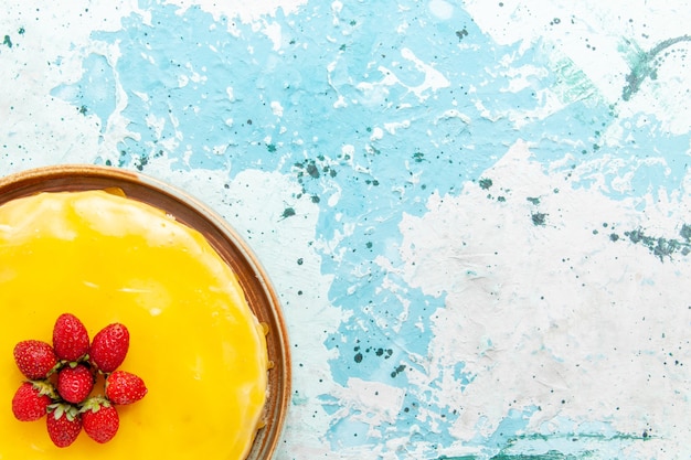Widok z góry pyszne ciasto z żółtym syropem i czerwonymi truskawkami na niebieskim biurku ciasto biszkoptowe słodkie ciasto cukrowe
