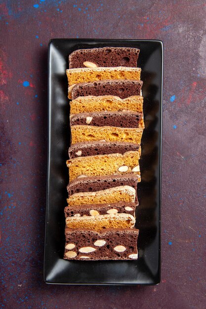Widok z góry pyszne pokrojone ciasto z orzechami wewnątrz formy do ciasta na ciemnym tle słodkie ciasto kakaowe biszkoptowe ciasteczka z cukrem