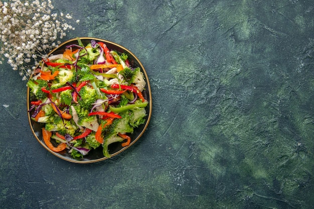 Widok z góry pysznej wegańskiej sałatki na talerzu z różnymi warzywami i białym widelcem po prawej stronie na ciemnym tle