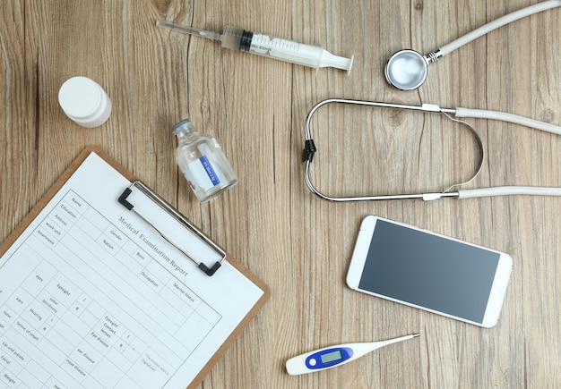 Widok z góry raportu z badań lekarskich, telefonu komórkowego i sprzętu medycznego na drewnianym biurku