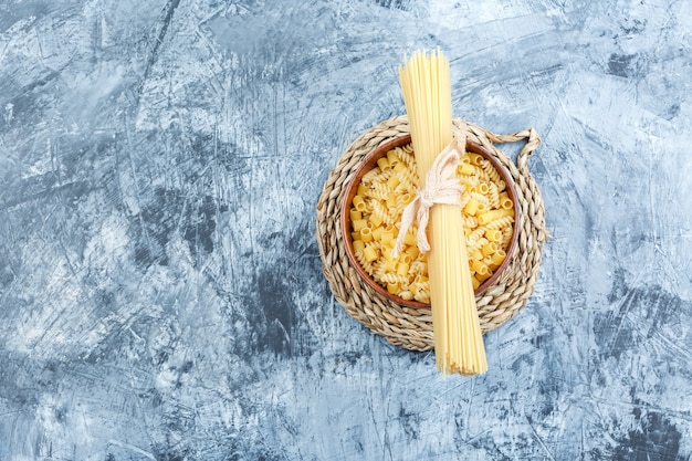 Bezpłatne zdjęcie widok z góry różne makarony w misce na tle szarego tynku i wikliny podkładka. poziomy