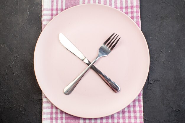 Widok z góry różowy talerz z widelcem i nożem na ciemnym tle