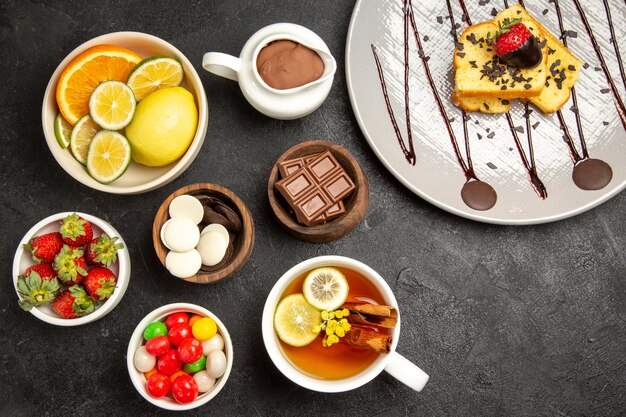 Widok z góry słodycze w miseczkach miski owoców cytrusowych cukierki czekoladowe truskawki krem czekoladowy talerz ciasta i filiżanka herbaty