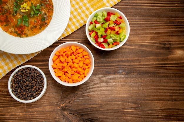 Widok z góry smaczna zupa jarzynowa z pokrojonymi warzywami na brązowym drewnianym biurku zupa jedzenie przyprawy warzywne