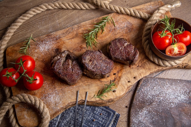 Widok z góry smażone smaczne mięso ze świeżymi czerwonymi pomidorami i zieleniną na drewnianym biurku posiłek jedzenie obiad mięso zdjęcie