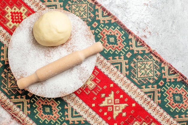 Bezpłatne zdjęcie widok z góry surowy kawałek ciasta z mąką na kolorowym dywanie i białym tle posiłek mąka piec ciasto