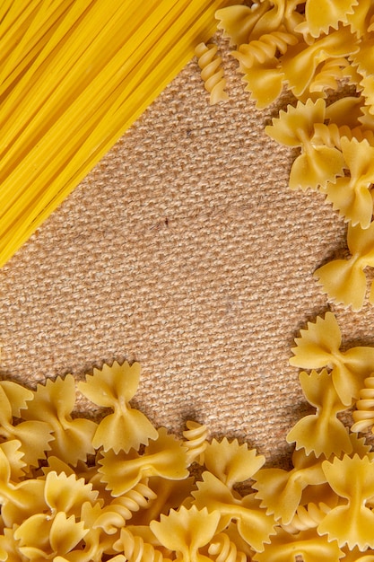 Widok z góry surowy włoski makaron, mały i długo uformowany, rozłożony na całej brązowej torbie makaronu włoskiego posiłku