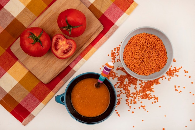 Widok z góry świeżej soczewicy na misce z pomarańczową zupą z soczewicy na misce z pomidorami na drewnianej desce kuchennej na kraciastej szmatce na białym tle