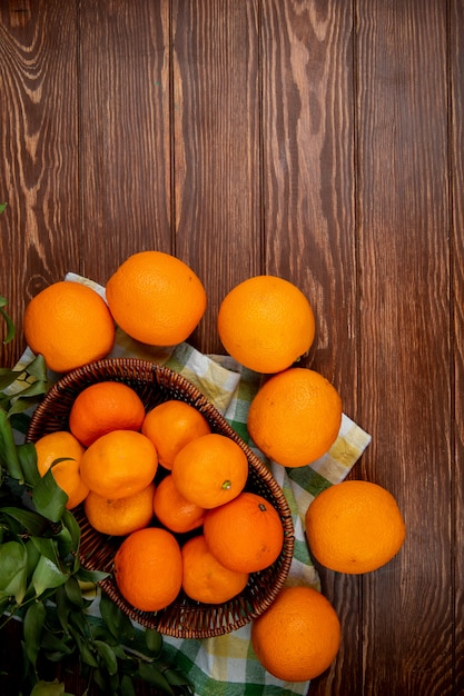 widok z góry świeżych mandarynek w wiklinowym koszu i dojrzałych pomarańczy na prosty drewniany stół z miejsca kopiowania
