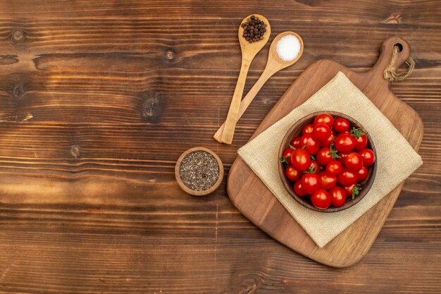 Widok z góry świeżych pomidorów na brązowej misce na desce do krojenia i przypraw w łyżkach pieprzu na drewnianej desce