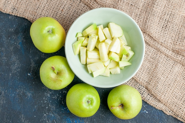 Bezpłatne zdjęcie widok z góry świeżych zielonych jabłek, soczystych i soczystych z pokrojonym jabłkiem wewnątrz talerza na ciemnym biurku, owoce świeże witamina zdrowia żywności
