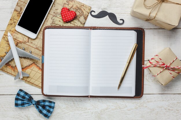 Widok z góry Szczęśliwy dzień ojca z travel.White telefon komórkowy i notebooka na tamtejsze drewniane background.accessories z, mapa, samolot, wąsy, zabytkowe krawat dziobu, długopis, obecne, czerwone serce.