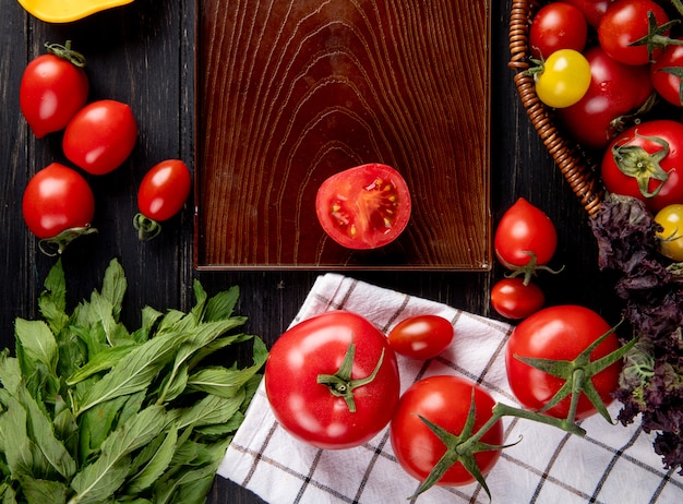 Widok z góry warzyw jako bazylia pomidorowa w koszu i pokrój pomidora na tacy z liśćmi zielonej mięty na drewnie