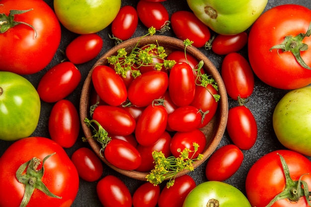 Widok z góry z bliska, wiśniowe, czerwone i zielone pomidory wokół miski z pomidorami cherry i kwiatami kopru na ciemnym podłożu