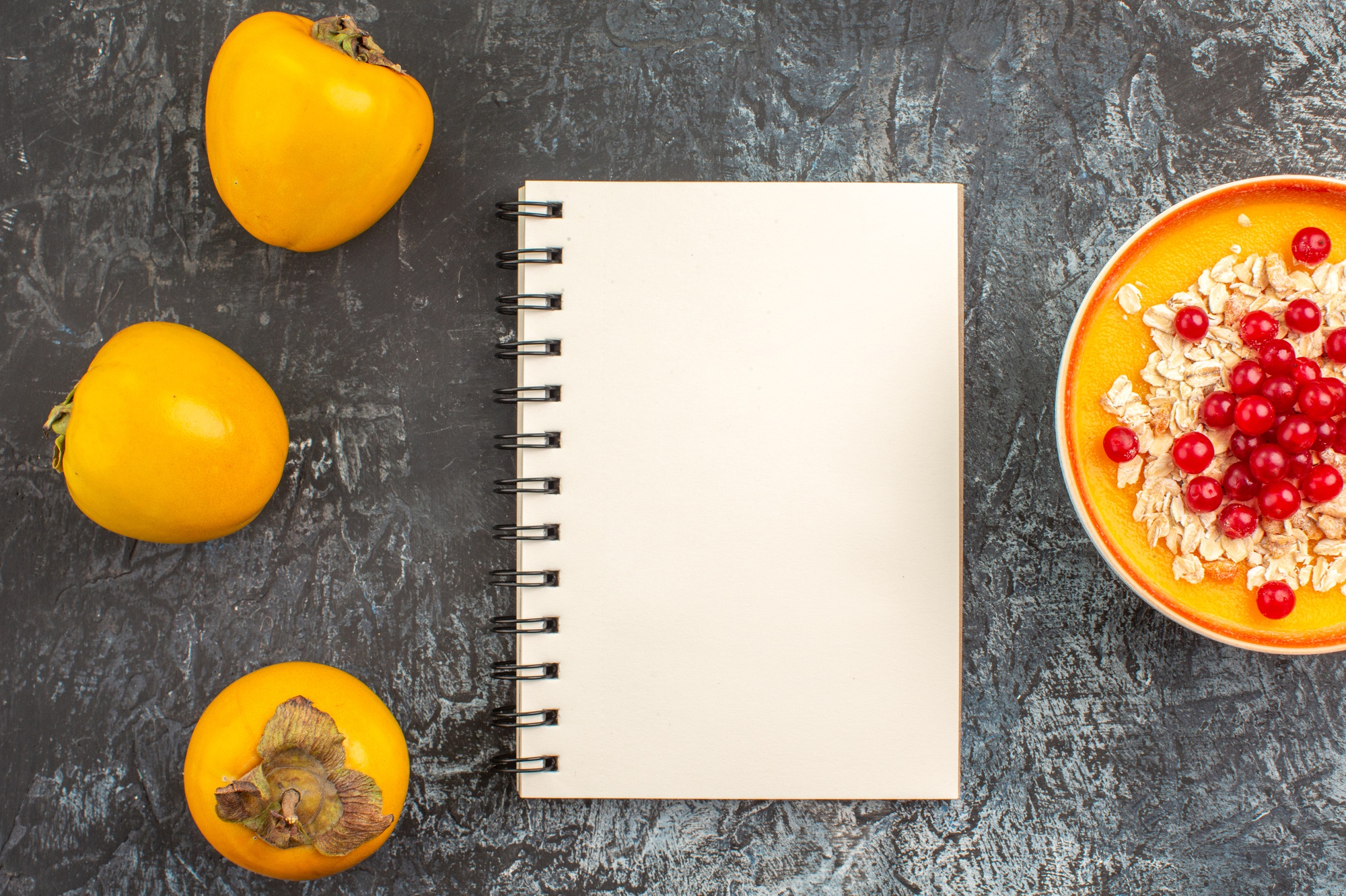 Widok z góry zbliżenie persimmons trzy persimmons miska z czerwonych porzeczek notebook