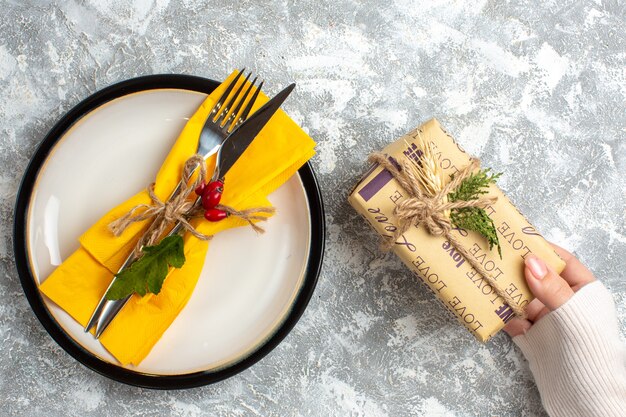 Bezpłatne zdjęcie widok z góry zestawu sztućców do posiłku na białym talerzu i dłoni trzymającej piękny zapakowany prezent na powierzchni lodu
